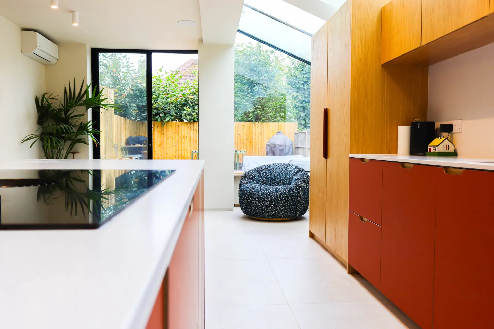 Bright kitchen extension with oak and terracotta cabinetry, large format floor tiles, black framed windows and a skylight overlooking the garden